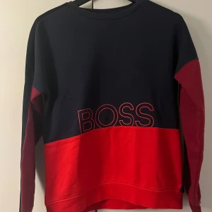 Hugo BOSS limited edition  sweatshirt i rött och marinblått - Snygg sweatshirt från BOSS i marinblått och rött med stor BOSS-logga framtill. Tröjan är limited edition och säljs inte längre, jag köpte den för 1800kr för 5-4 år sedan men  är bara andvänd ett fåtal gånger. Skick 9,5/10, finns inga tecken på andvänding!