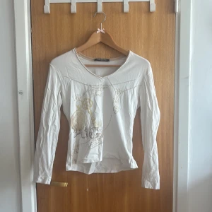 Vit långärmad topp Betty Barclay - Vit långärmad topp från Betty Barclay med v-ringning och snyggt tryck i guld och beige framtill. Tunt och mjukt bomullsmaterial, perfekt för dig som gillar stilrena detaljer och en feminin look. Passar till jeans eller kjol💗