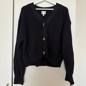 Svart stickad kofta från H&M - Svart stickad kofta från H&M i storlek S. Koftan har v-ringning, stora dekorativa knappar framtill och långa ärmar. Den är ribbstickad och har en lite loose passform, perfekt att slänga över en t-shirt eller linne.