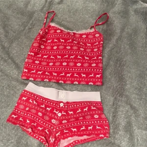 Röd julig linnetopp med renar - Supersöt röd linnetopp med smala axelband och vitt julmönster med renar och snöflingor. Toppen har spetsdetalj upptill och är perfekt för mysiga vinterkvällar. Matchar shortsen på bilden för en komplett look.