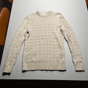 Beige kabelstickad tröja Selected Homme - Säljer en beige kabelstickad tröja från Selected Homme i storlek M. Tröjan har klassiskt kabelmönster, rund halsringning och ribbade muddar vid ärmslut och nederkant. Perfekt för lager-på-lager under kyliga dagar.