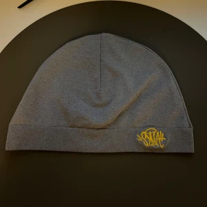 Grå mössa med gul brodyr från Syna - Snygg grå mössa i mjuk bomull med gul broderad Stay-logga framtill. Enkel och stilren design som passar perfekt till streetwear. Mössan har en klassisk passform och är riktigt skön att bära.den är f3ek men ser bra ut 👍