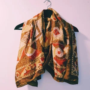 Mönstrad halsduk i varma färger - Snygg halsduk med unikt mönster i brunt, beige, rött och gult. Tunt och mjukt material som känns skönt mot huden. Perfekt accessoar för att lyfta din outfit med lite extra färg och stil.  Små hål finns annars fint skick