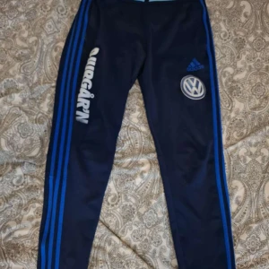 Adidas träningstights blå herr - Mörkblå träningstights från Adidas med blå ränder längs sidorna och tryck av Volkswagen och AIK-logga. Tight passform och elastiskt material som passar perfekt för sport eller gym. Klassisk Adidas-design med logga på låret.
