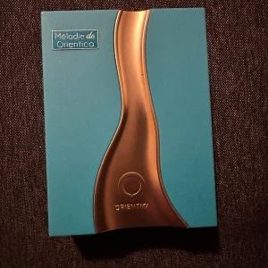 Mélodie de Orientica Eau de Parfum - Snygg parfym från Orientica i en turkos och guldig förpackning. Flaskan har en unik, vågformad design med guldiga detaljer och ett T-format lock. Kommer i en lyxig box som matchar flaskans färg. Perfekt för dig som gillar stilrena och moderna dofter.