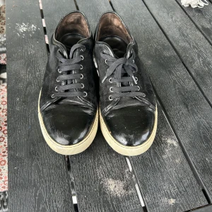 Svarta sneakers från Lanvin i skinn och mocka  - Snygga svarta sneakers från Lanvin med ovandel i en mix av skinn och mocka. Skorna har svarta snören, rund tå och vit platt sula med Lanvin-logga undertill. Perfekta för dig som gillar stilrena och exklusiva sneakers med en lyxig känsla. Bara skor kommer med Storlek 43.