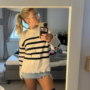 Randig stickad tröja i offwhite och marinblå - Säljer en oversized stickad tröja i offwhite med breda marinblå ränder. Tröjan har rund halsringning, långa ärmar och ribbade muddar samt slits i sidorna. Perfekt för en chill och stilren look.