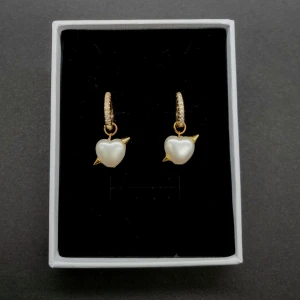 Guldörhängen med pärlhjärtan - Supersöta örhängen i guld med vita hjärtformade pärlor och små gulddetaljer. Hängena har glittriga stenar på ringen och hjärtat har en cool spetsig detalj. Perfekta för att ge din look lite extra edge och romantisk vibe.