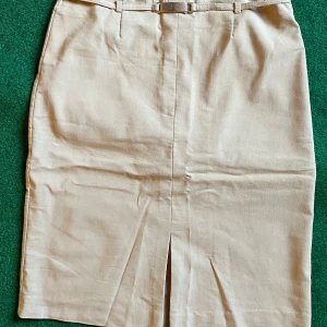 Beige pennkjol från Fransa, stl 40 - Snygg beige pennkjol från Fransa med klassisk passform och bälte i midjan. Kjolen har slits framtill för extra rörelsefrihet och är perfekt för en clean och stilren look. Passar dig som gillar enkel och tidlös stil.