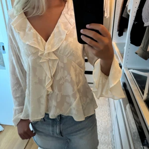 Blommig volangblus från Zara - Supersöt ljusbeige blus från Zara med blommigt mönster i tyget. Blusen har v-ringning, volangdetaljer längs halsringningen och framtill samt vida ärmar. Storlek L men sitter bra på mig som vanligtvis bär xs/s
