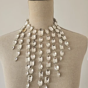 Statement halsband med stora kristaller - Superglittrigt statement halsband med stora, rektangulära och ovala klara kristaller i flera rader som hänger ner över bröstet. Halsbandet har silverfärgad kedja och ger en riktigt lyxig och iögonfallande look..obs saknas en sten