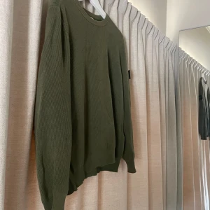 Olivgrön stickad tröja Stone Island - Säljer en olivgrön stickad tröja från Stone Island med klassisk patch på ärmen. Tröjan har rund hals, ribbade muddar och lång ärm. Perfekt för dig som gillar streetwear och vill ha något stilrent men ändå fett. Materialet är mjukt och ger en skön passform. Köpte den i Milano för 3200kr ny.
