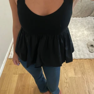 Svart ärmlös linnetopp med volang - Supersnygg svart linnetopp med breda axelband och volangig, utställd nederdel💗