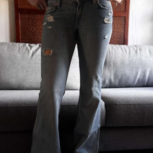 Weekday Nova Low Slim Bootcut Jeans - Säljer ett par Weekday Nova Low Slim Bootcut jeans i ljusblå denim med slitna detaljer och hål för en cool, avslappnad vibe. Låg midja och bootcut-ben ger en snygg siluett. Perfekta för dig som gillar en trendig och edgy look.