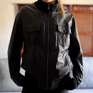 Svart skinnjacka från Batistini M - Svart skinnjacka från Batistini i storlek medium. Jackan har två stora bröstfickor, ribbad hög krage och muddar samt dragkedja framtill. Snygg och tidlös modell som ger en cool vibe till din outfit. Perfekt för höst och vinter!