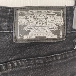 Svarta jeans från Crocker - Svarta jeans från Crocker med klassisk femficksdesign och raka ben. Jeansen har en snygg tvättad finish och tydliga sömmar. Perfekta för dig som gillar en enkel och stilren look. Materialet är slitstarkt denim.