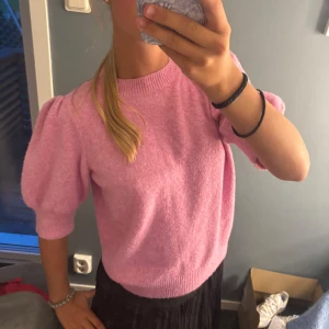 Rosa stickad tröja från Vero Moda - Superfin rosa stickad tröja från Vero Moda med puffärmar och ribbade muddar. Tröjan har en rund halsringning och är i en mjuk, mysig kvalitet. Perfekt för dig som gillar en söt och trendig look med lite volym på ärmarna.