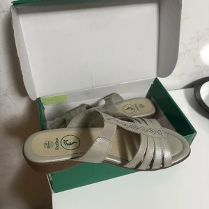 Beige sandaler med strass från FootFlexx - Snygga beige sandaler från FootFlexx med flera remmar och dekorativa strassdetaljer på ovandelen. Skorna har en låg klack, öppen tå och bekväm platt sula. Perfekta för varma dagar och ger en stilren look till din outfit.