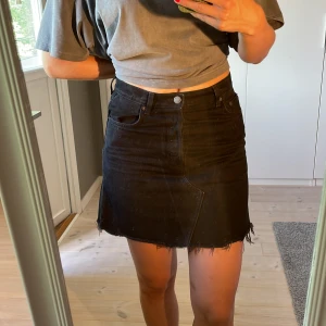 Svart jeanskjol med fransig kant - Svart kort jeanskjol med något högre midja och rå, fransig nederkant. Snygg och enkel att styla till olika outfits.