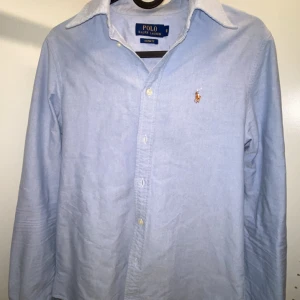 Ljusblå skjorta från Polo Ralph Lauren - Klassisk ljusblå skjorta från Polo Ralph Lauren i custom fit. Skjortan har lång ärm, knappar framtill och den ikoniska broderade loggan på bröstet. Perfekt för dig som gillar stilrena och tidlösa plagg. Tillverkad i mjuk bomull för en skön känsla. Den är snarare slimfit än custom fit. Är du mellan XS-S? Då passar denna skjortan dig perfekt. Har du några funderingar, skriv till mig😆