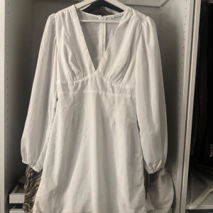 Vit kortklänning med v-ringning - Superfin vit kortklänning från NA-KD med djup v-ringning och långa ärmar. Klänningen har en markerad midja och lätt puffiga ärmar för en trendig look. Perfekt för sommarens alla tillfällen!