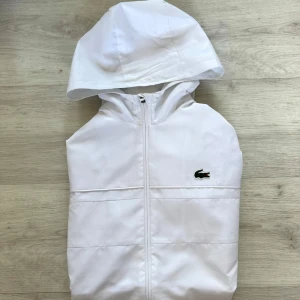 Lacoste vindjacka windbreaker - Snygg vit vindjacka från Lacoste Sport med huva och dragkedja framtill. Knappast använd. Dunderskick.