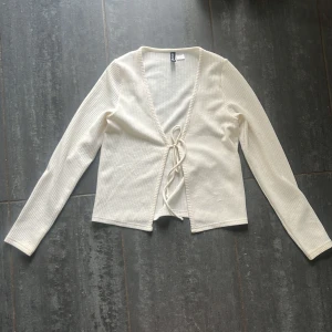 Vit ribbad omlottopp från H&M Divided - Säljer en vit ribbad omlottopp från H&M Divided i storlek S. Toppen har långa ärmar, v-ringning och knyt framtill. 
