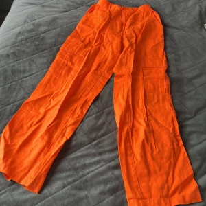 Orange cargopants från H&M Divided - Snygga orange cargopants från H&M Divided i 100% bomull. Byxorna har bred resår i midjan, stora sidofickor och en loose passform med raka ben. Perfekta för dig som vill sticka ut med färg och ha gott om plats för prylar.