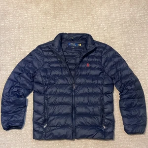 Mörkblå dunjacka Polo Ralph Lauren M - Säljer nu denna mörkblå dunjacka från Polo Ralph Lauren. Skicket är bra förutom en liten skada vid back sida axel(se sista bilden) men de påverkar inte funktionen. Ny pris ca 4000! Vid minsta lilla fundering är de bara att höra av sig. 