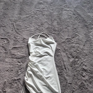 Vit satin kortklänning med snörning - Supersnygg vit kortklänning i satin med tunna axelband som korsas i ryggen. Glansigt matrial, klänningen är köpt från shein. Inte använd för mycket då den är lite genomskinlig. 
