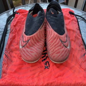 Nike Phantom GX fotbollsskor röd/svart - Nike Phantom GX fotbollsskor i rött och svart med vita detaljer och swirl-mönster. Skorna har en strumpliknande passform utan snörning, med syntetiskt material och tydliga Swoosh-loggor på sidorna. Perfekta för dig som vill sticka ut på planen.