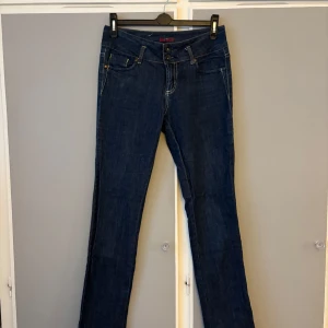 Mörkblå stretchjeans från Bik Bok - Snygga vintage mörkblå stretchjeans från Bik Bok med klassisk femficksdesign och dubbla knappar i midjan. Jeansen har raka ben och är tillverkade i bomull med lite elastan för extra komfort. Perfekta för dig som gillar en tidlös och enkel look.