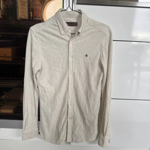 Morris skjorta - Snygg randig skjorta från Morris i storlek XS. Skjortan har klassisk krage, knäppning framtill och diskret logga broderad på bröstet. Tillverkad i mjuk bomull och passar perfekt till jeans eller chinos.