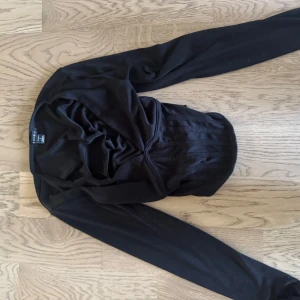 Svart långärmad topp från Amisu - Svart långärmad topp från Amisu med snyggt åtsittande midja och draperad detalj framtill. Toppens material är mjukt och stretchigt, perfekt för en stilren look. Passformen är normal och den har en klassisk rund halsringning.