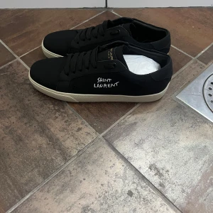 Saint laurent skor - Svarta sneakers från Saint Laurent med vit sula och broderad logga på sidan. Skorna har snörning, rund tå och är tillverkade i canvas och skinn. Klassisk och stilren design med diskreta detaljer och Saint Laurent Paris-tryck på plösen och sulan. och vid en snabb afär går de att diskutera priset