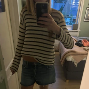 Randig stickad tröja från Zara - Säljer en beige och svart randig stickad tröja från Zara. Tröjan har lång ärm, rund hals och en loose fit som ger en chill vibe. Perfekt till jeans eller shorts för en avslappnad look. Materialet är mjukt och andas, vilket gör den skön att bära.