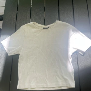 Vit ribbad topp från LMTD - Enkel och stilren vit ribbad topp från LMTD. Modellen har rund halsringning och korta ärmar, perfekt för en clean och avslappnad look. Tunt och mjukt material som känns skönt mot huden. Passar till allt och är lätt att matcha med andra plagg.