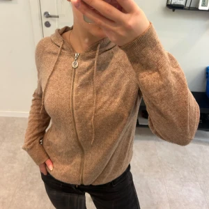 Beige kofta från Edblad - Mysig beige hoodie från Edblad med hel dragkedja och huva. Tröjan är stickad och har långa ärmar samt snygga detaljer i form av snörning vid huvan och en metall-logga på dragkedjan. Perfekt att hänga över sig nu till sommaren eller som lager på lager till hösten och vintern🥰🥰