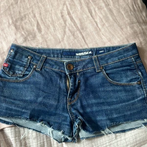 Jeansshorts från Miss Sixty, stl 29 - Snygga blå jeansshorts från Miss Sixty med fransiga kanter och klassiska fickor både fram och bak. Shortsen har låg midja. Midjemått: 40cm