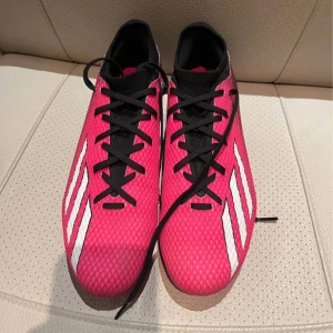 Adidas rosa och svarta fotbollsskor - Snygga fotbollsskor från Adidas i en grymt cool rosa och svart färg med vita ränder på sidorna. Skorna har snörning, mönstrad ovandel i syntet och dobbar för bästa grepp på planen. Perfekta för dig som vill sticka ut på matchen! Kan diskutera pris 