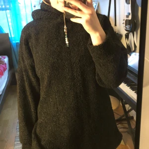 Svart oversized teddy hoodie - Mysig svart hoodie i teddyfleece med oversized passform och lång ärm. Tröjan har huva och en cool slits baktill som ger extra edge. Perfekt för kalla dagar när du vill vara både bekväm och stilren.