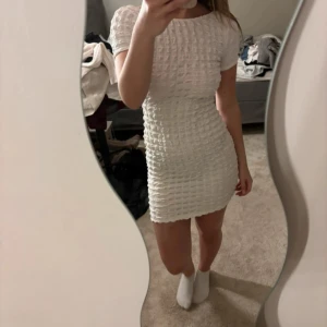 Vit kort klänning Pull & Bear - Supersöt vit kort klänning från Pull & Bear med strukturerat tyg och öppen rygg. Den har korta ärmar och en tight passform som framhäver figuren. Perfekt för dig som vill sticka ut med en stilren look och coola detaljer.