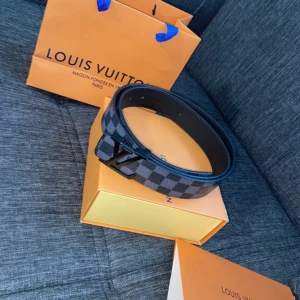 Louis Vuitton rutig skärp i skinn - Snyggt Louis Vuitton bälte i svart och grått med klassiskt rutigt Damier-mönster. Bältet har en stilren LV-spänne i svart och är tillverkat i exklusivt skinn. Perfekt accessoar för att lyfta din outfit med en lyxig touch.