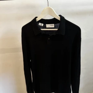 Svart pikétröja från Selected Homme - Klassisk svart pikétröja från Selected Homme med krage och knappslå. Tröjan är långärmad och har en stilren, enkel design som passar perfekt till jeans eller chinos. Tillverkad i mjukt material för en bekväm känsla hela dagen.