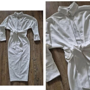 Vit skjortklänning med knytband - Snygg vit långklänning med skjortkrage, långa ärmar och knytband i midjan. Klänningen har knappar framtill och är figurnära med en stilren look. Perfekt för dig som gillar minimalistisk stil och vill ha något som sticker ut men ändå känns klassiskt.