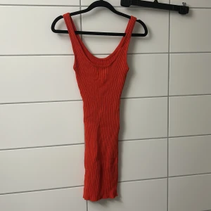 Ribbad röd ärmlös kortklänning - Snygg röd ribbad klänning med tight passform och breda axelband. Modellen är ärmlös och har en rundad halsringning. Perfekt för dig som gillar en enkel men ändå iögonfallande stil.