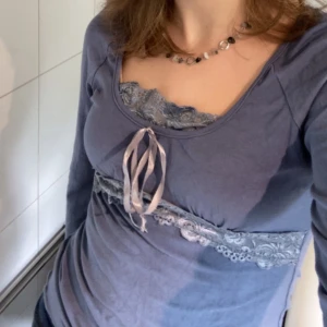 Ljusblå topp med spets och snörning - Supersöt ljusblå långärmad topp med spetsdetaljer vid urringningen och under bysten. Snygg snörning framtill som ger en feminin vibe. Mjuk och stretchig bomullsmix, perfekt till jeans eller kjol. Figurnära passform med utsvängda armar för en romantisk känsla.