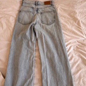 Ljusblå wide jeans från Gina tricot - Säljer ett par ljusblå jeans från Gina i modell med breda ben och hög midja. Klassisk femficksdesign, dragkedja och knapp framtill. Perfekta för en chill och trendig look.