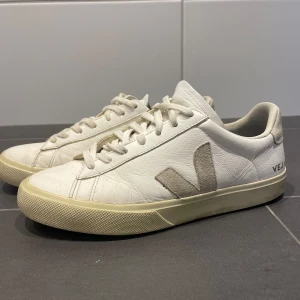 Vita sneakers från Veja i skinn - Stilrena vita sneakers från Veja med klassisk låg profil och rund tå. Skorna har snörning, beige sula och V-logga i mocka på sidan. Tillverkade i skinn med detaljer i mocka för en clean och tidlös look.