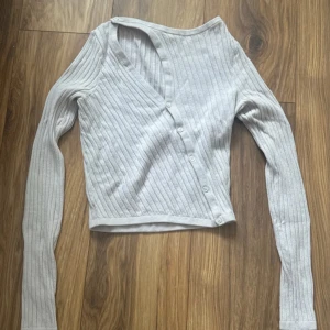 Gråbeige  ribbad kofta från & Other Stories - Supersnygg gråbeige ribbad kofta från & Other Stories. Koftan har v-ringning, knappar framtill och är långärmad. Perfekt att slänga över en topp eller bära stängd. Mjuk och skön i bomullsmix, passar till allt. Hör av er vid frågor 💕